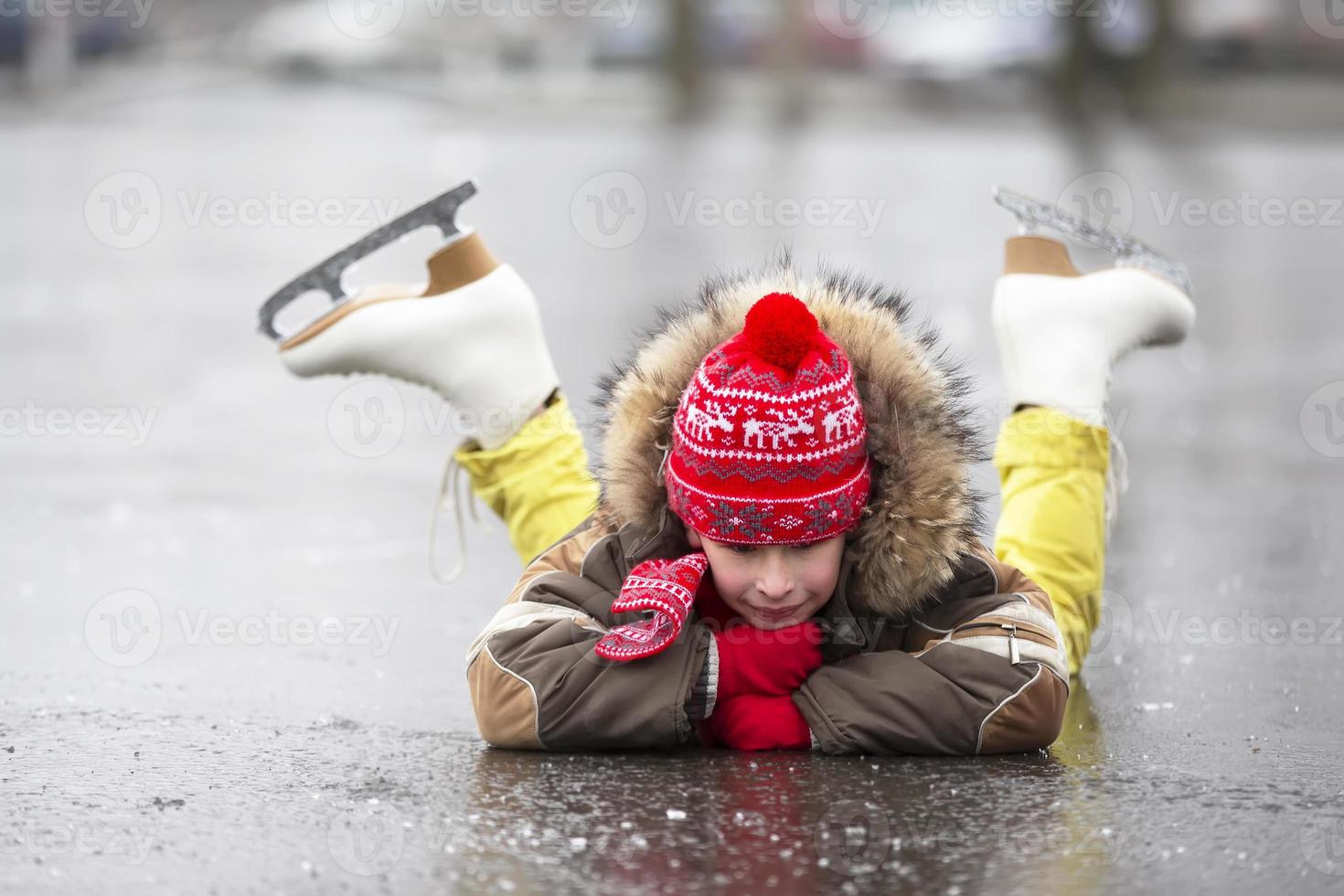 A child in figure skates in winter lies on the ice and smiles. photo