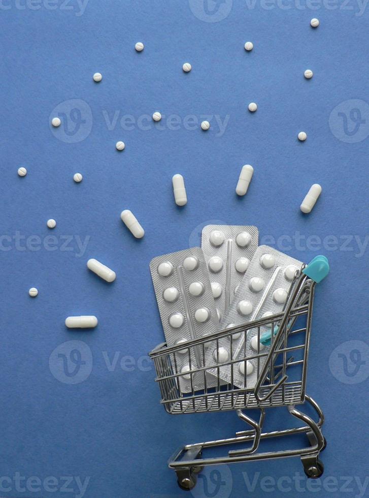 Shopping cart with medicine pills in pack on classic blue background with copy space. Creative idea for drugstore, online pharmacy, health lifestyle and pharmaceutical company business concept. photo