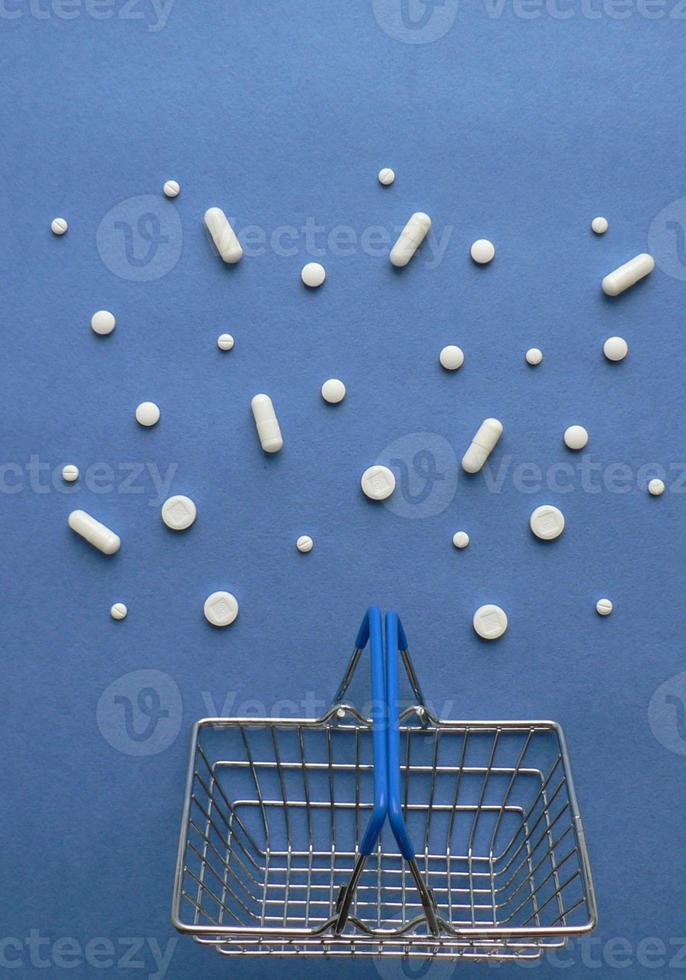 Shopping cart with medicine pills in pack on classic blue background with copy space. Creative idea for drugstore, online pharmacy, health lifestyle and pharmaceutical company business concept. photo