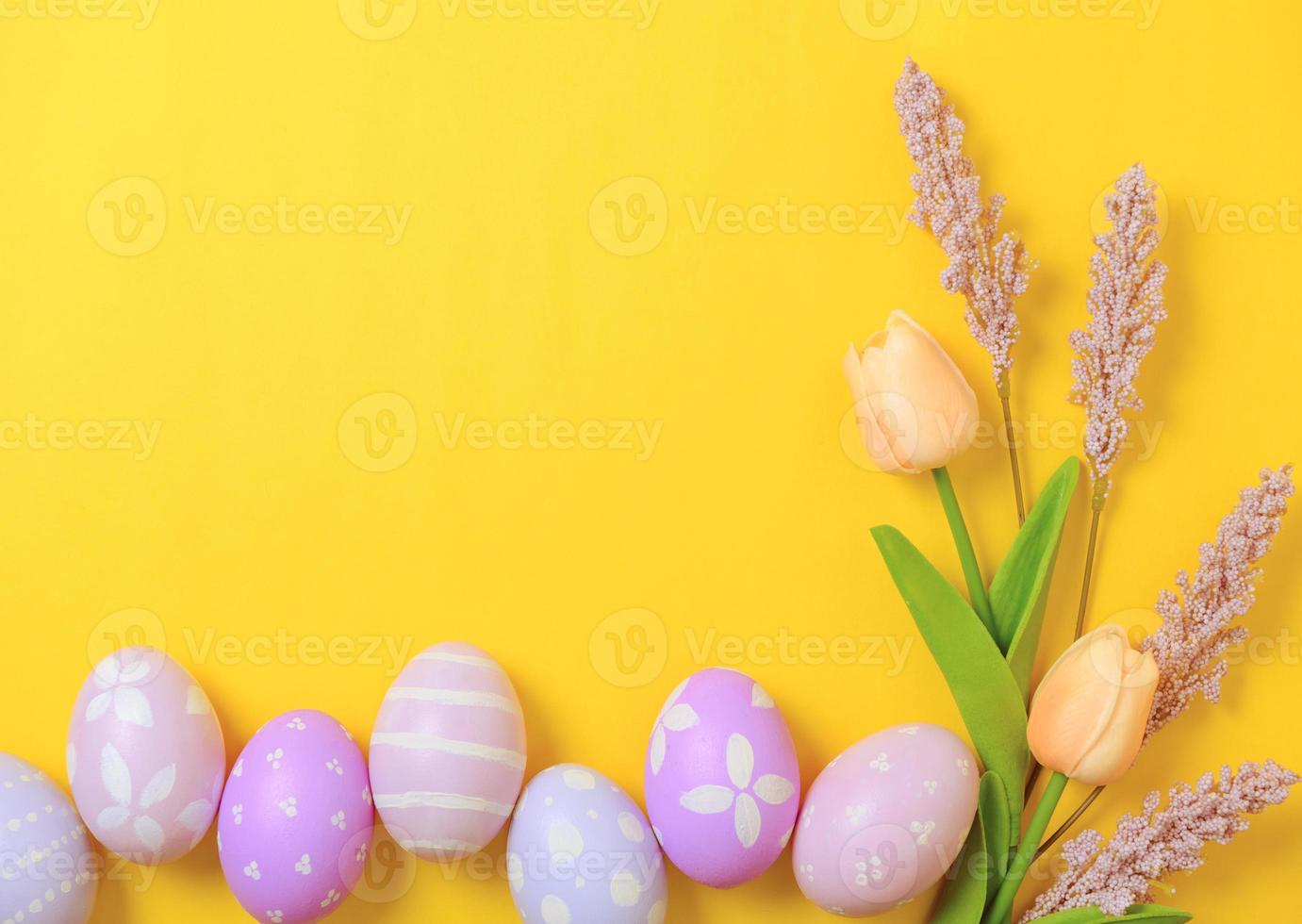 Happy Easter holiday greeting card design concept. Colorful Easter Eggs and spring flowers on yellow background. Flat lay, top view, copy space. photo