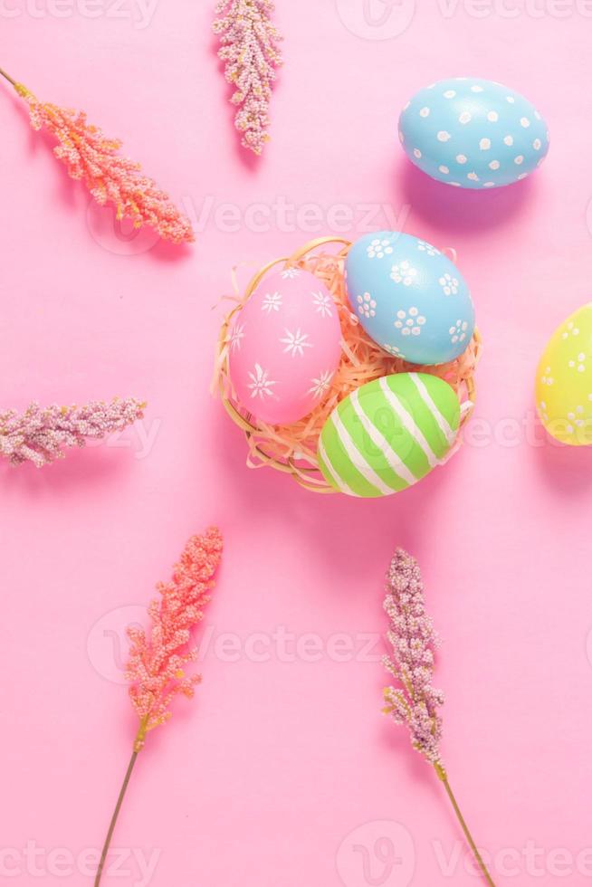 Happy Easter holiday greeting card concept. Colorful Easter Eggs and spring flowers on pastel pink background. Flat lay, top view, copy space. photo
