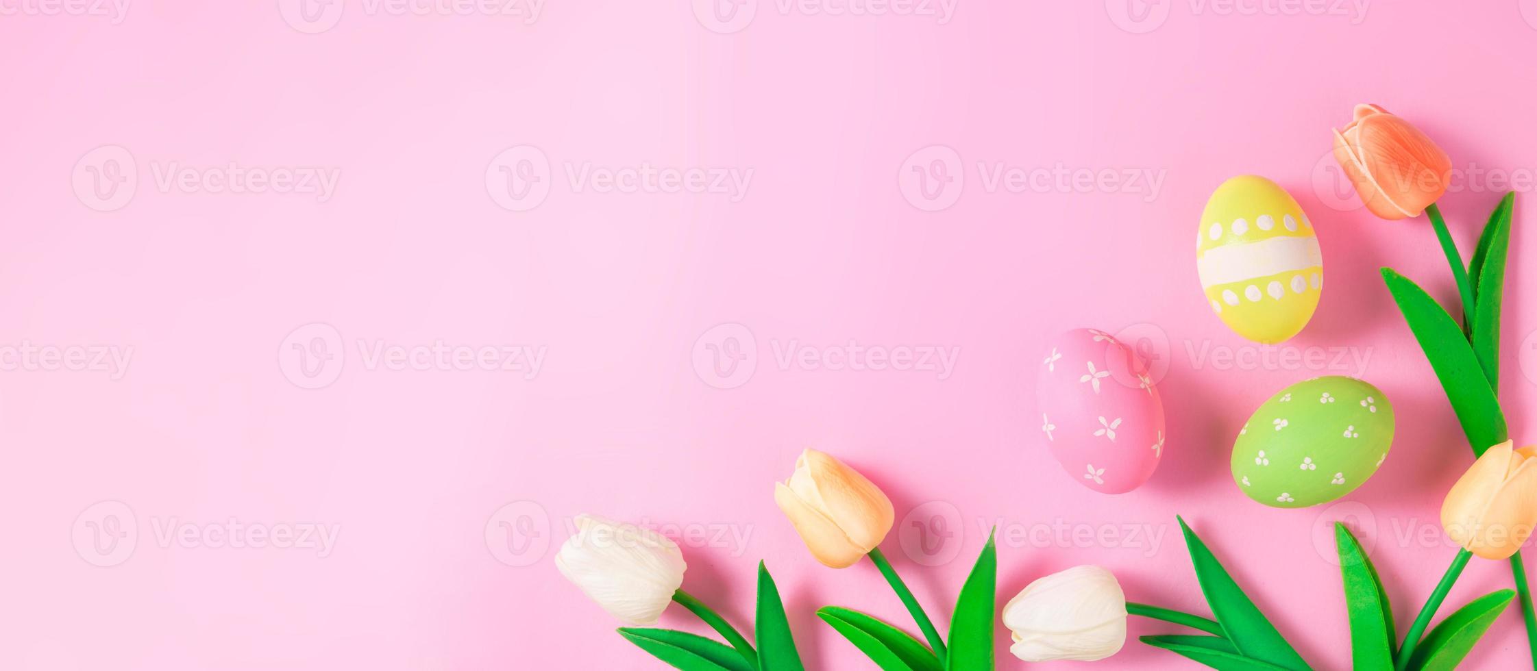 Happy Easter holiday greeting card concept. Colorful Easter Eggs and spring flowers on pastel pink background. Flat lay, top view, copy space. photo