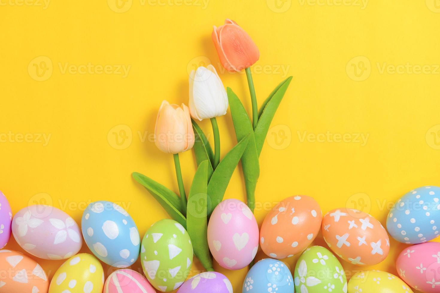Happy Easter holiday greeting card design concept. Colorful Easter Eggs and spring flowers on yellow background. Flat lay, top view, copy space. photo