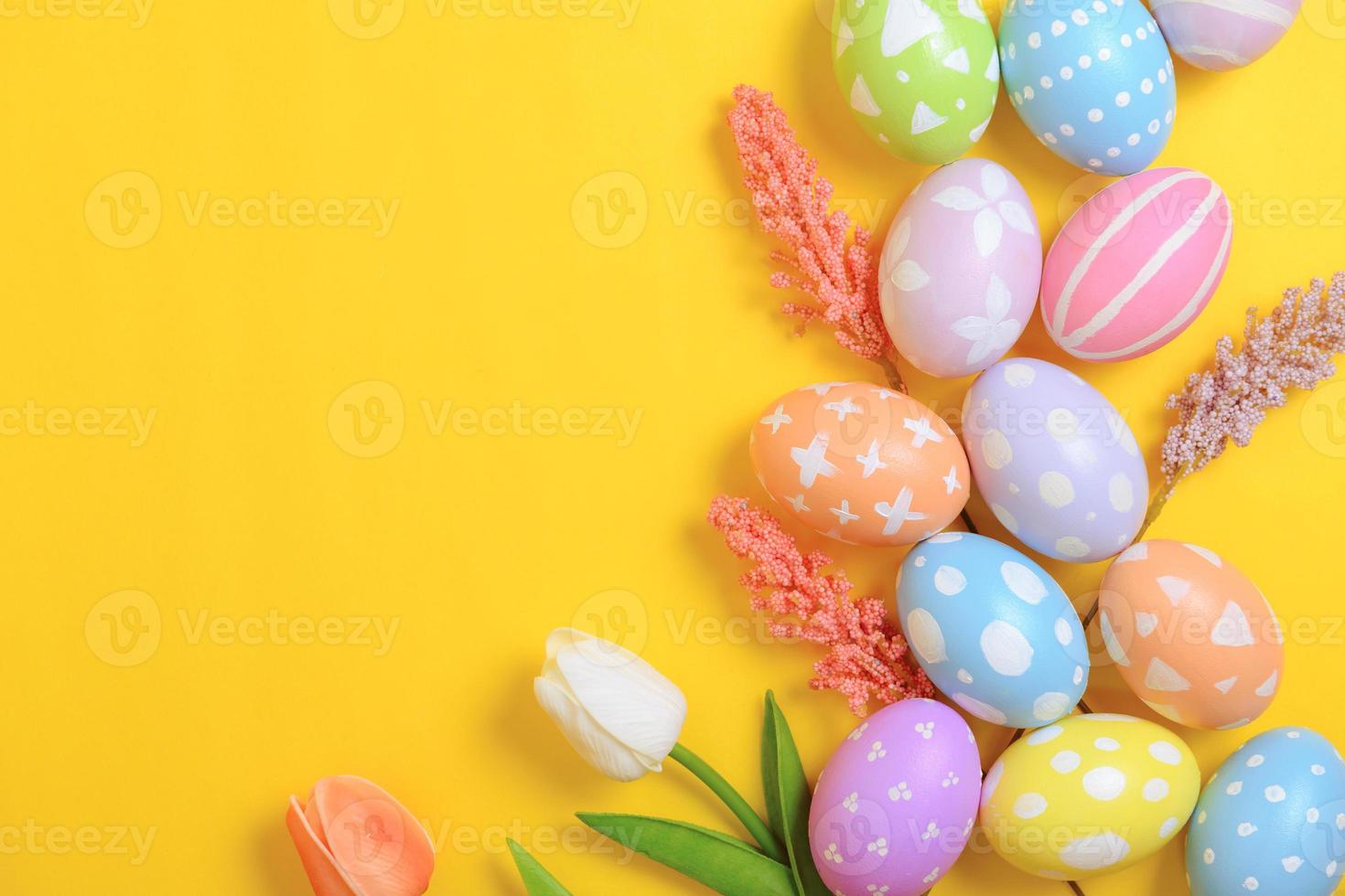 Happy Easter holiday greeting card design concept. Colorful Easter Eggs and spring flowers on yellow background. Flat lay, top view, copy space. photo