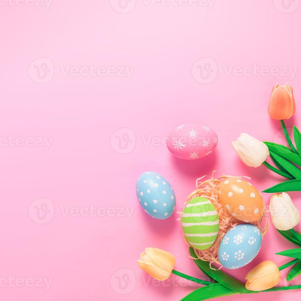 Happy Easter holiday greeting card concept. Colorful Easter Eggs and spring flowers on pastel pink background. Flat lay, top view, copy space. photo