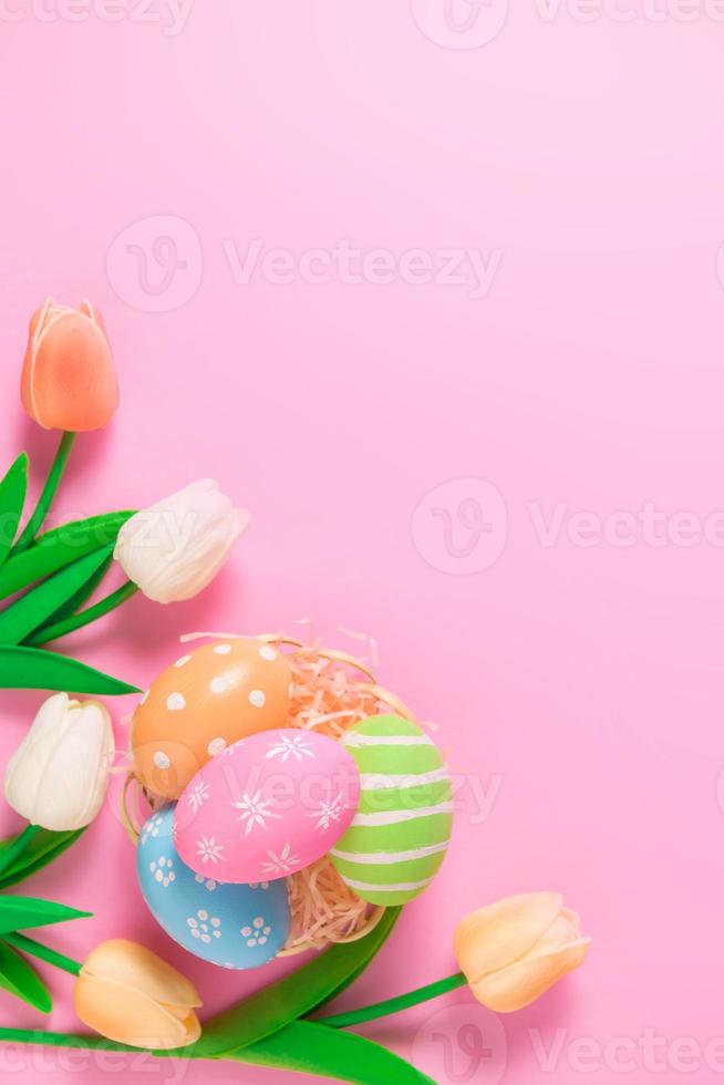 Happy Easter holiday greeting card concept. Colorful Easter Eggs and spring flowers on pastel pink background. Flat lay, top view, copy space. photo