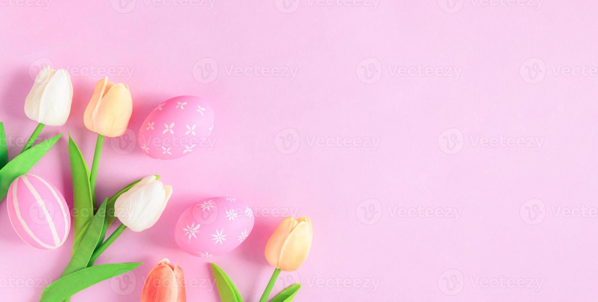Happy Easter holiday greeting card concept. Colorful Easter Eggs and spring flowers on pastel pink background. Flat lay, top view, copy space. photo