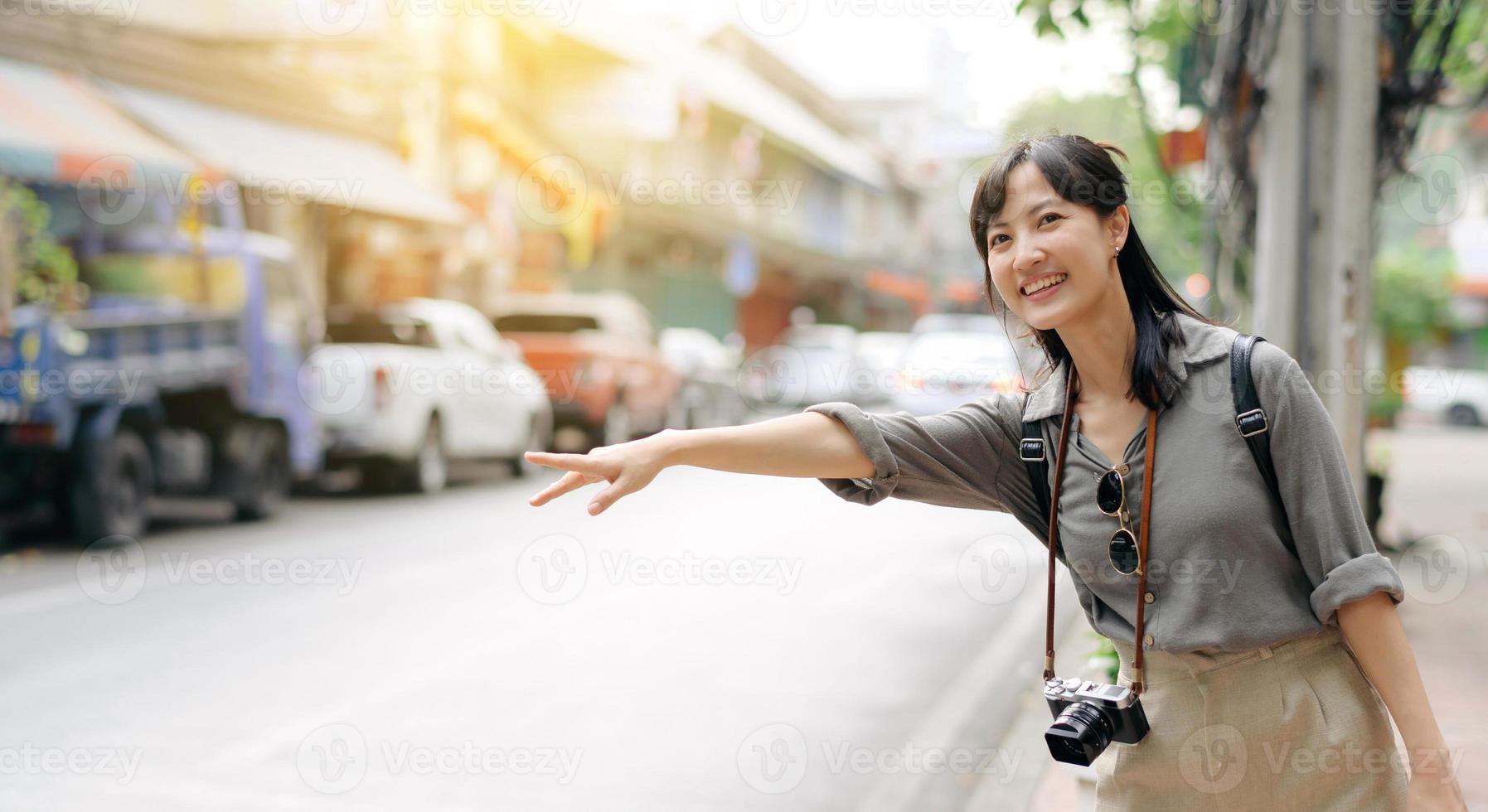 sonriente joven asiático mujer viajero autoestop en un la carretera en el ciudad. vida es un viaje concepto. foto