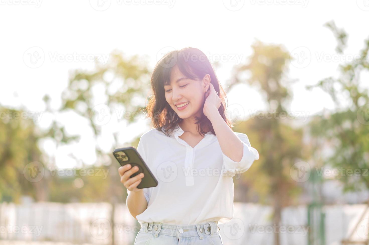 retrato hermosa joven asiático mujer con inteligente móvil teléfono alrededor al aire libre naturaleza ver en un soleado verano día foto