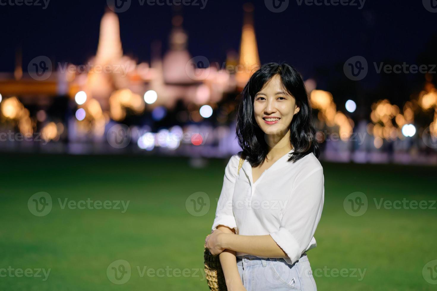Portrait young beautiful asian woman smiling while travel at Temple of the Emerald Buddha or Wat Phra Kaew in night view point, Bangkok, Thailand. photo