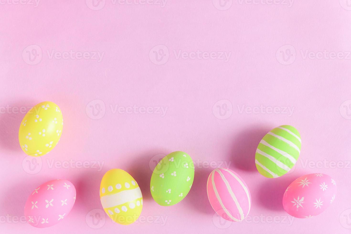 Happy Easter holiday greeting card concept. Colorful Easter Eggs and spring flowers on pastel pink background. Flat lay, top view, copy space. photo