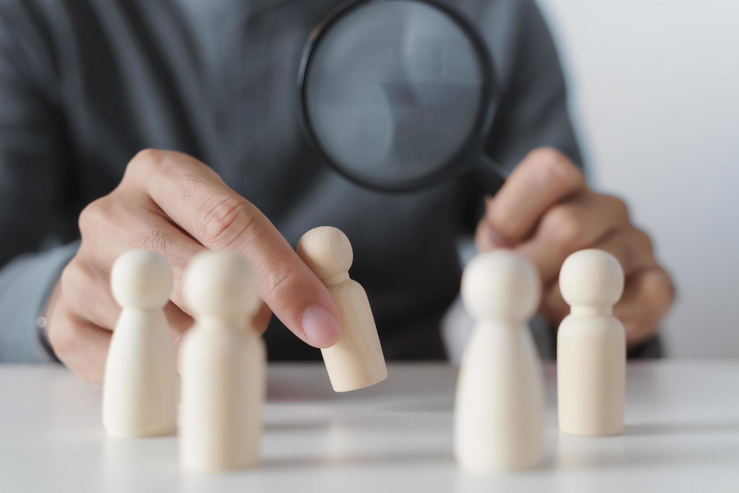 mano sosteniendo una lupa centrándose en la figura de madera. búsqueda de empleo, recursos humanos, concepto de contratación foto