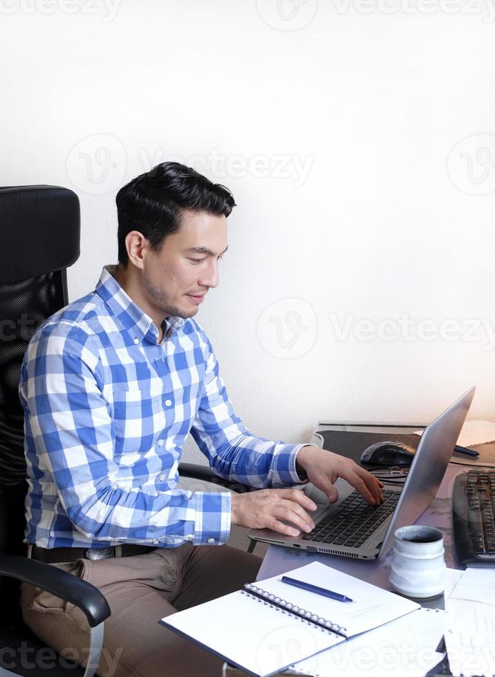 un hombre en un comprobado camisa trabajando desde hogar a un escritorio foto