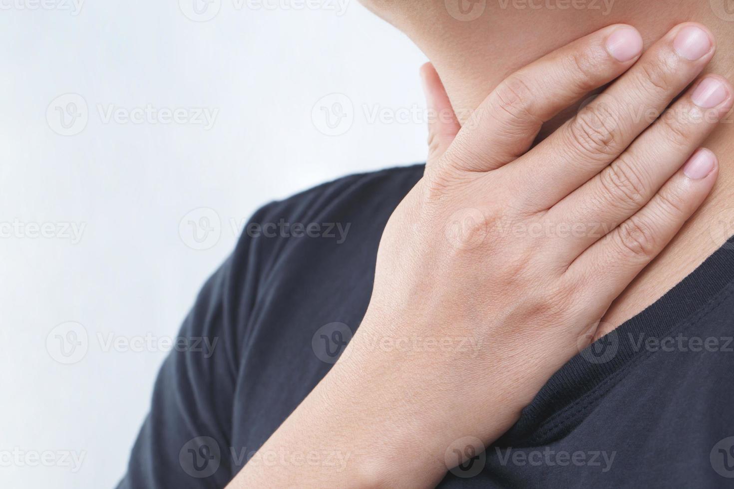 sore throat pain. Closeup of young man sick holding her inflamed throat using hands to touch the ill neck in blue shirt on gray background. Medical and healthcare concept. Focus red on to show pain. photo