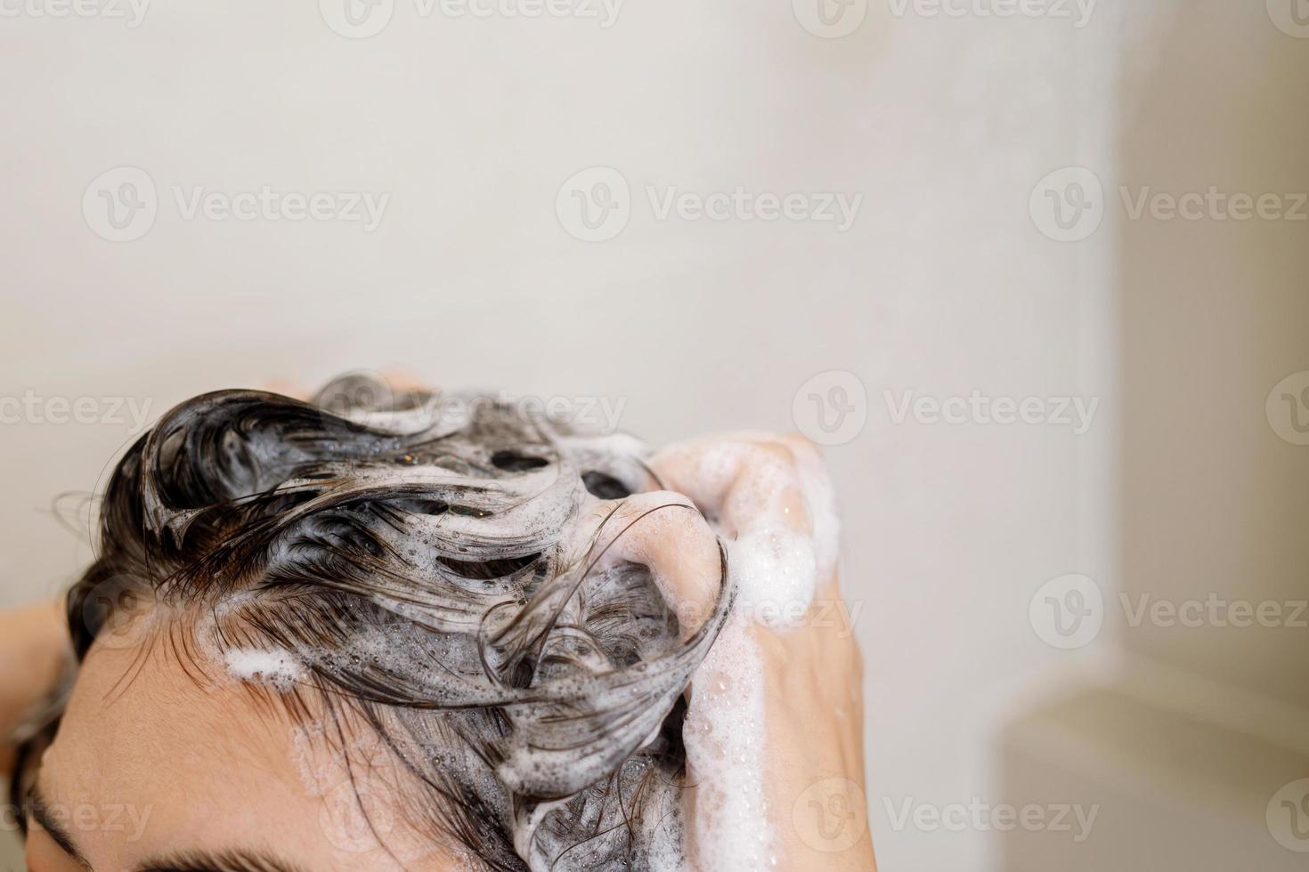 Woman taking shower and washing hair with shampoo in bathroom at home photo