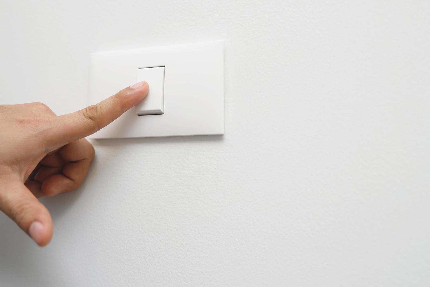 apague la luz, cierre la mano del hombre del dedo está cerrando el interruptor de encendido con la pared en casa para ahorrar energía. reducir el calentamiento global. foto