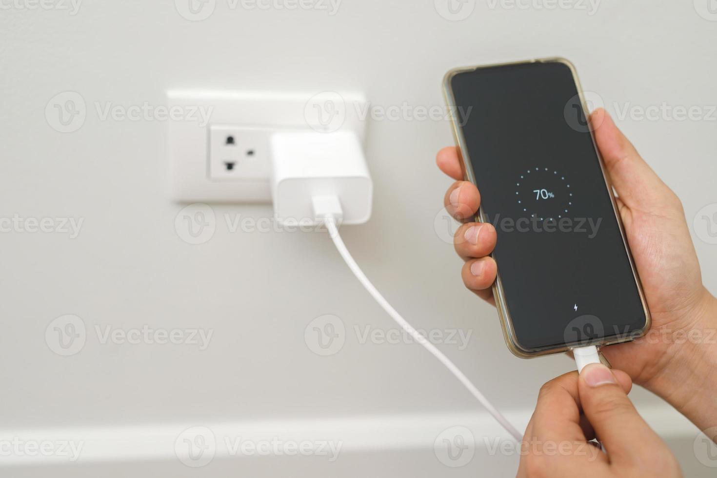 close up hand plugging adapter charge the battery with outlet socket plug and hold mobile phone on wall ,electric safety concept photo