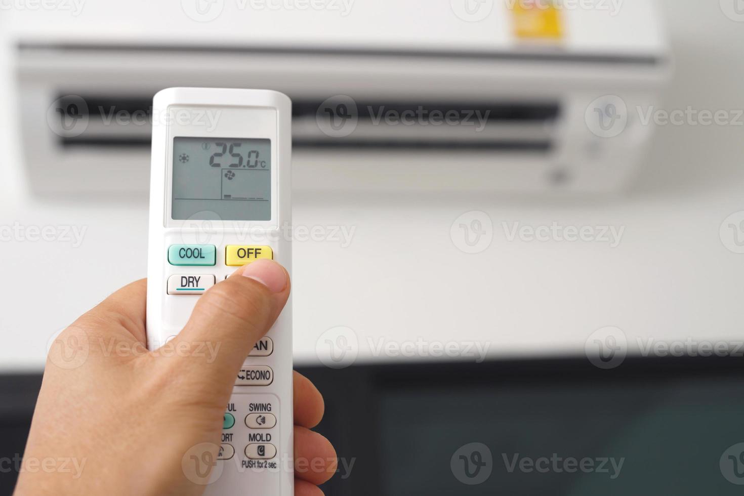 Air conditioner inside the room with close up man hand holding using directed operating remote controller. photo