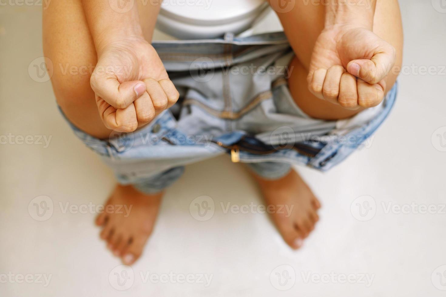 Cropped image of man sitting excrete on toilet. His jeans is hanging on his legs in toilet. photo