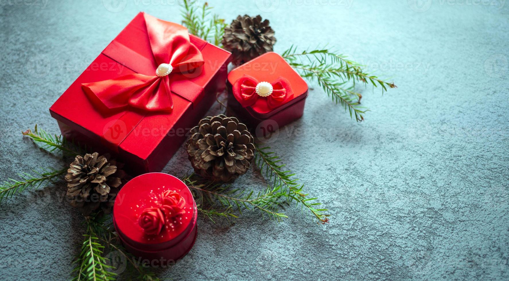 Christmas decoration composition on gray concrete background with a beautiful Red gift box with red ribbon, tree branches, and pine cones photo