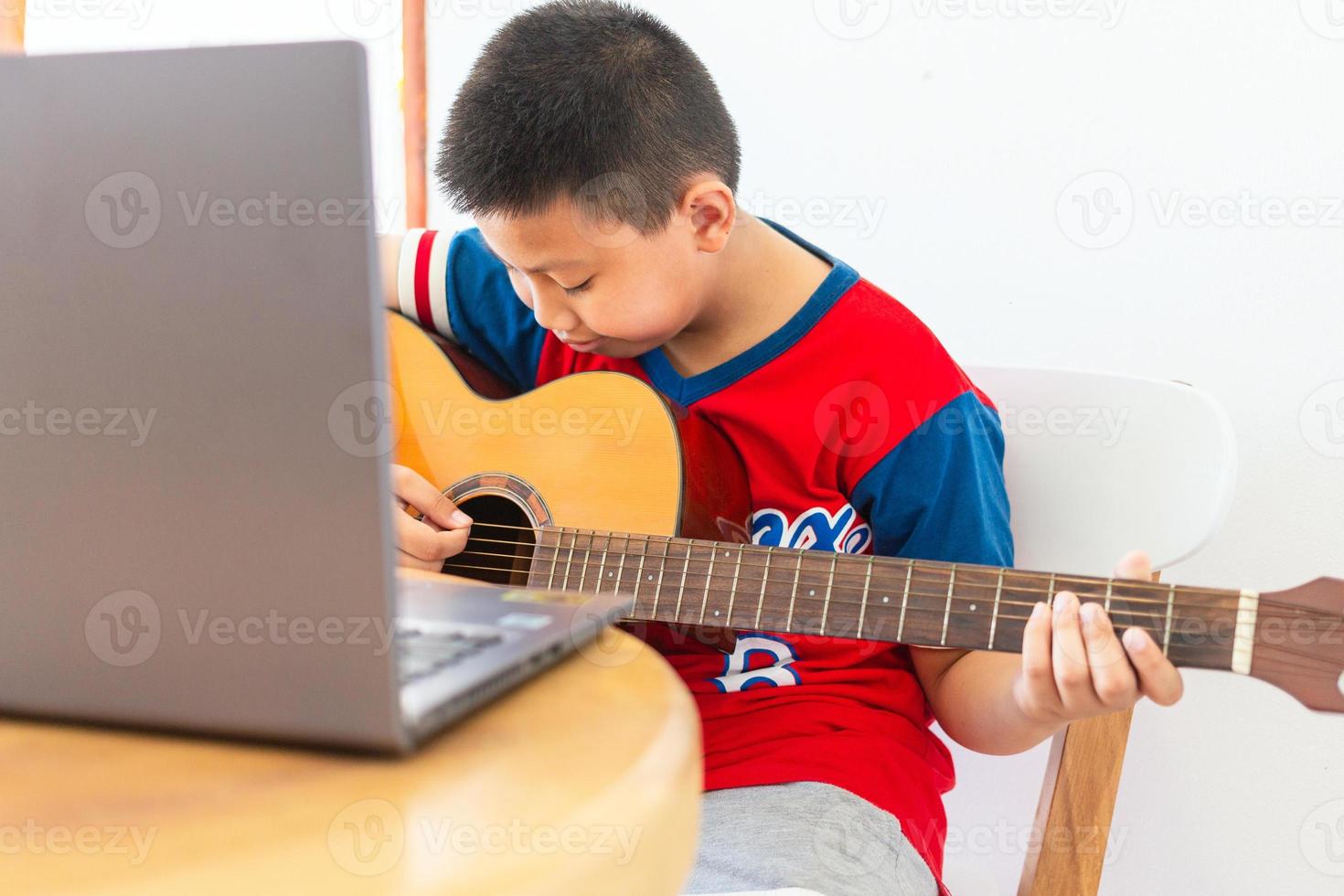 The story of a boy watching a notebook computer while preparing to practice playing guitar at home. Boys take classical guitar lessons online. photo