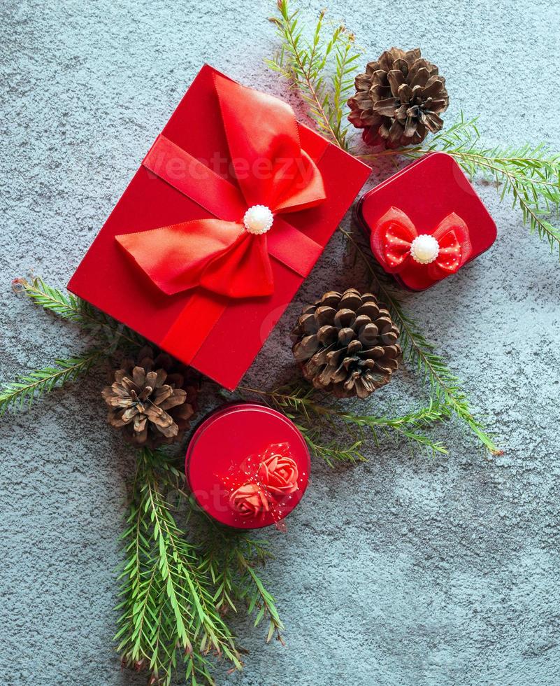 Christmas decoration composition on gray concrete background with a beautiful Red gift box with red ribbon, tree branches, and pine cones photo