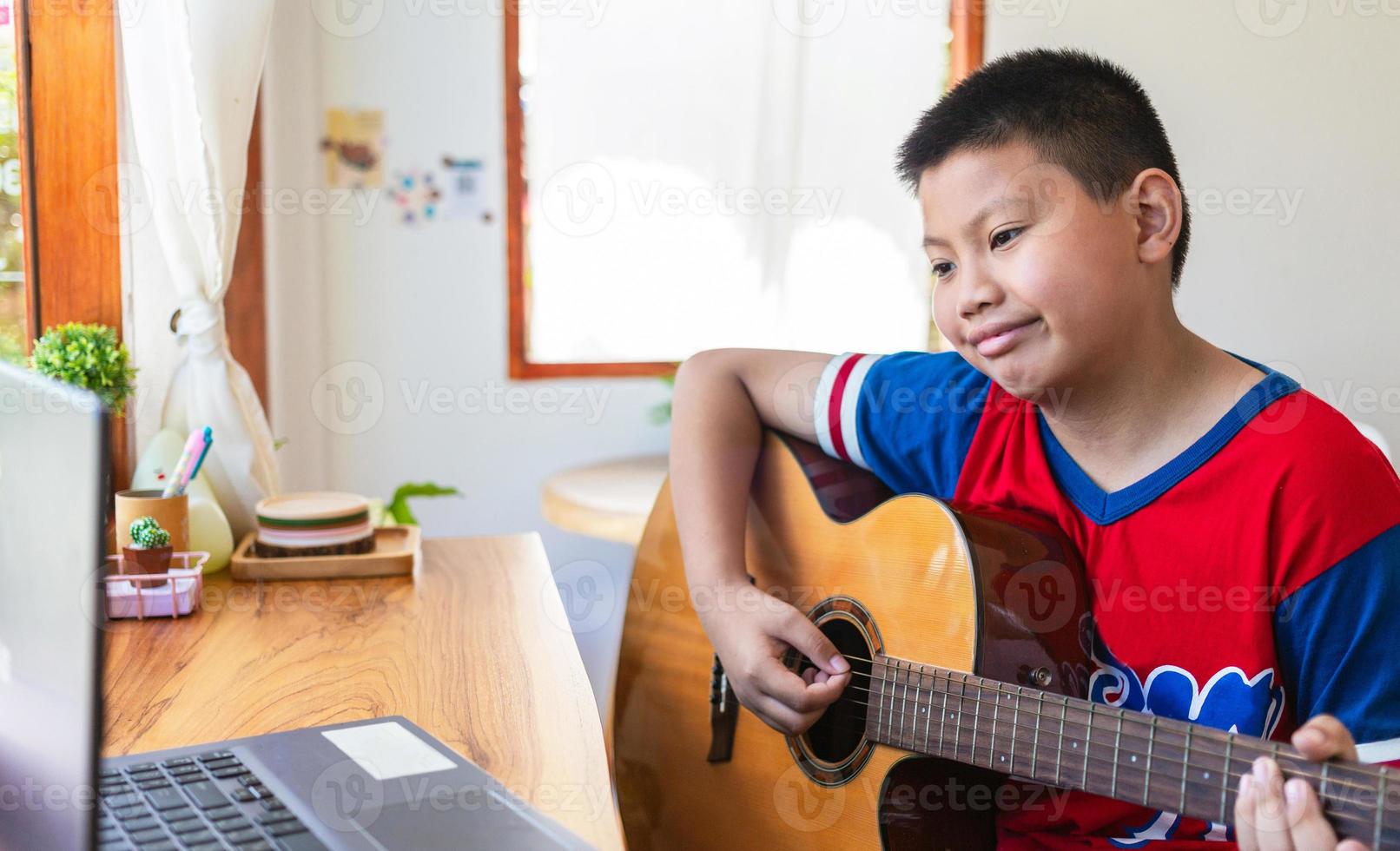 The story of a boy watching a notebook computer while preparing to practice playing guitar at home. Boys take classical guitar lessons online. photo