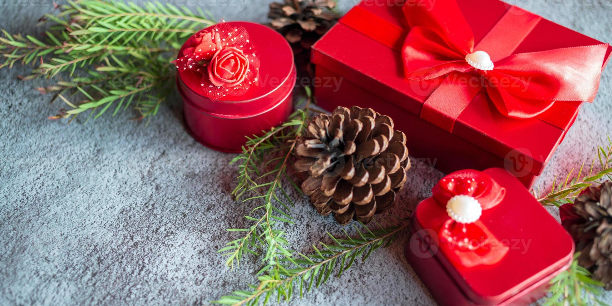 Christmas decoration composition on gray concrete background with a beautiful Red gift box with red ribbon, tree branches, and pine cones photo