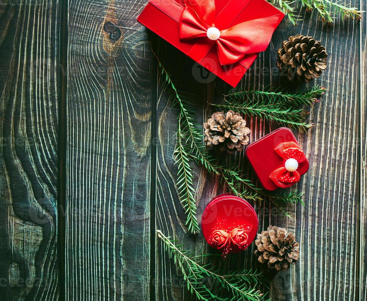 Christmas decoration composition on wooden background with a beautiful Red gift box with red ribbon, tree branches, and pine cones photo