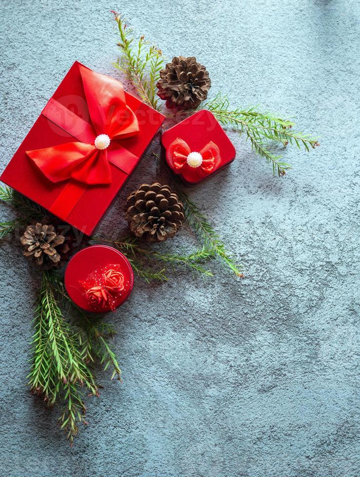 Christmas decoration composition on gray concrete background with a beautiful Red gift box with red ribbon, tree branches, and pine cones photo