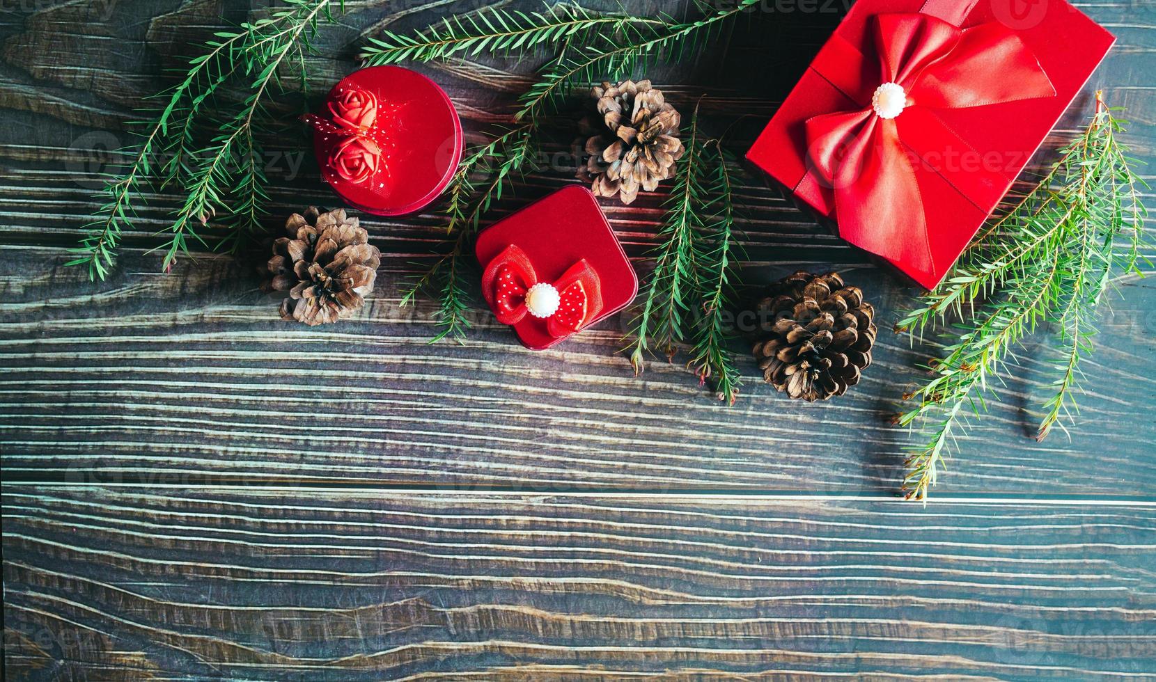 Christmas decoration composition on wooden background with a beautiful Red gift box with red ribbon, tree branches, and pine cones photo