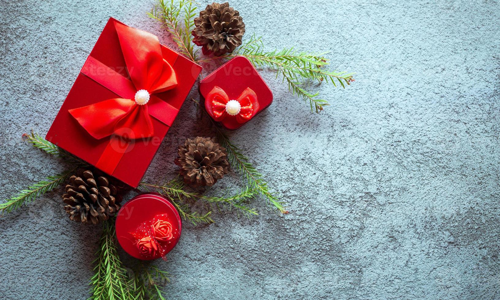 Christmas decoration composition on gray concrete background with a beautiful Red gift box with red ribbon, tree branches, and pine cones photo