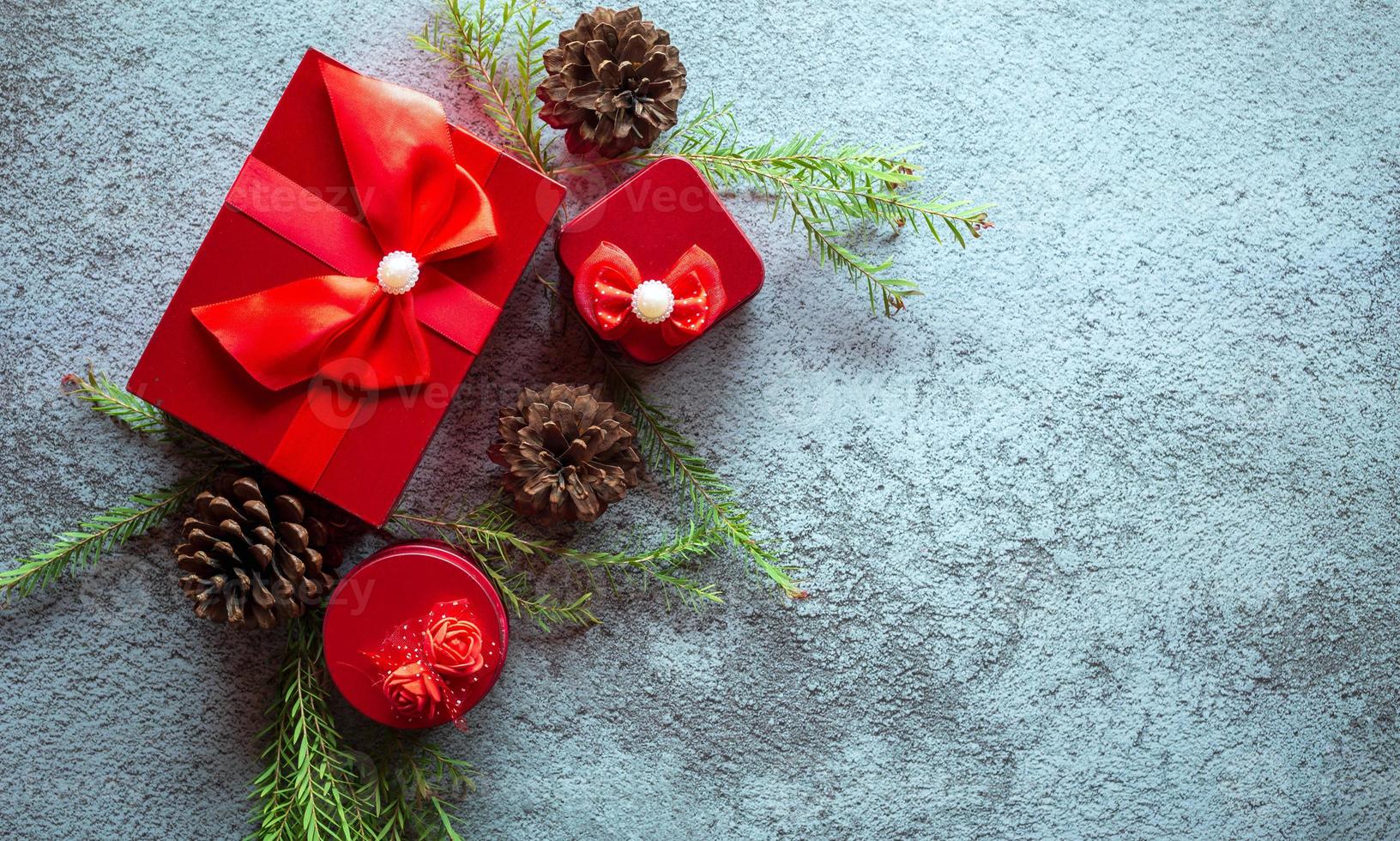 Navidad decoración composición en gris hormigón antecedentes con un hermosa rojo regalo caja con rojo cinta, árbol sucursales, y pino conos foto