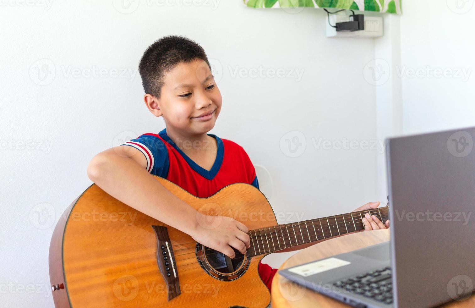 The story of a boy watching a notebook computer while preparing to practice playing guitar at home. Boys take classical guitar lessons online. photo