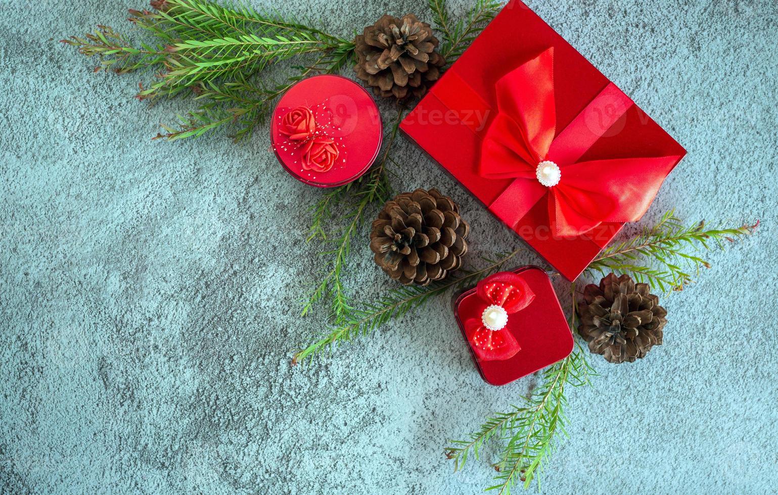 Christmas decoration composition on gray concrete background with a beautiful Red gift box with red ribbon, tree branches, and pine cones photo