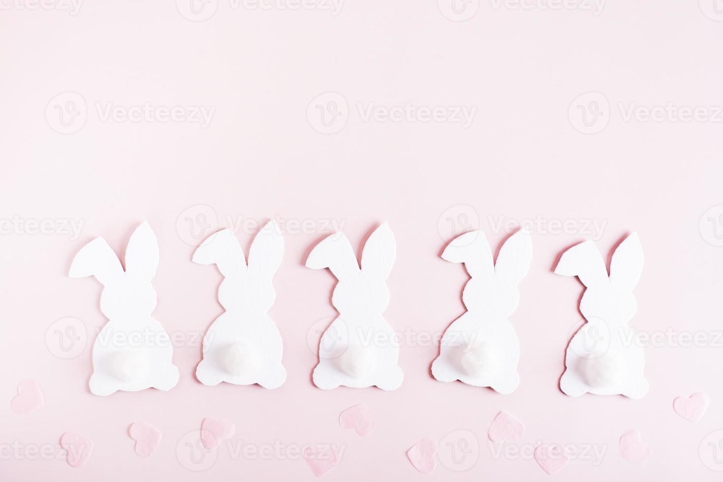 Happy easter white cardboard bunnies in a row and hearts on pink background top view photo