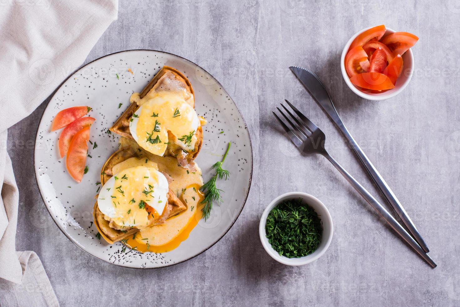 Eggs benedict and bacon on a crispy waffle on a plate for homemade breakfast. Top view photo