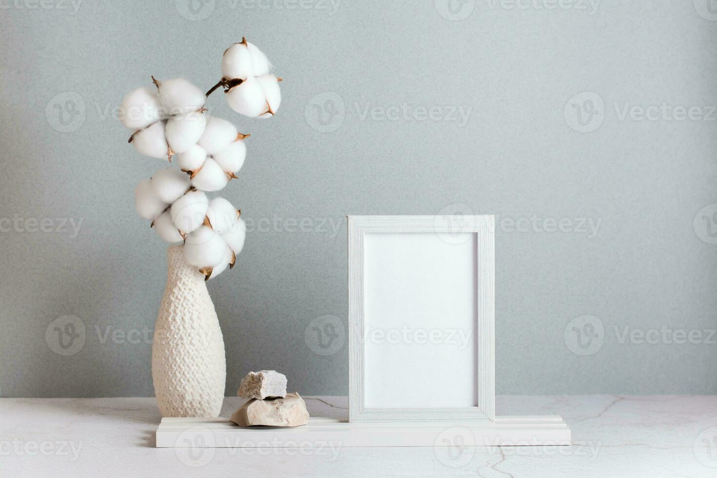 eco simpático hogar decoración algodón rama en un florero, foto marco y piedras en el mesa en un gris antecedentes. pastel sombras