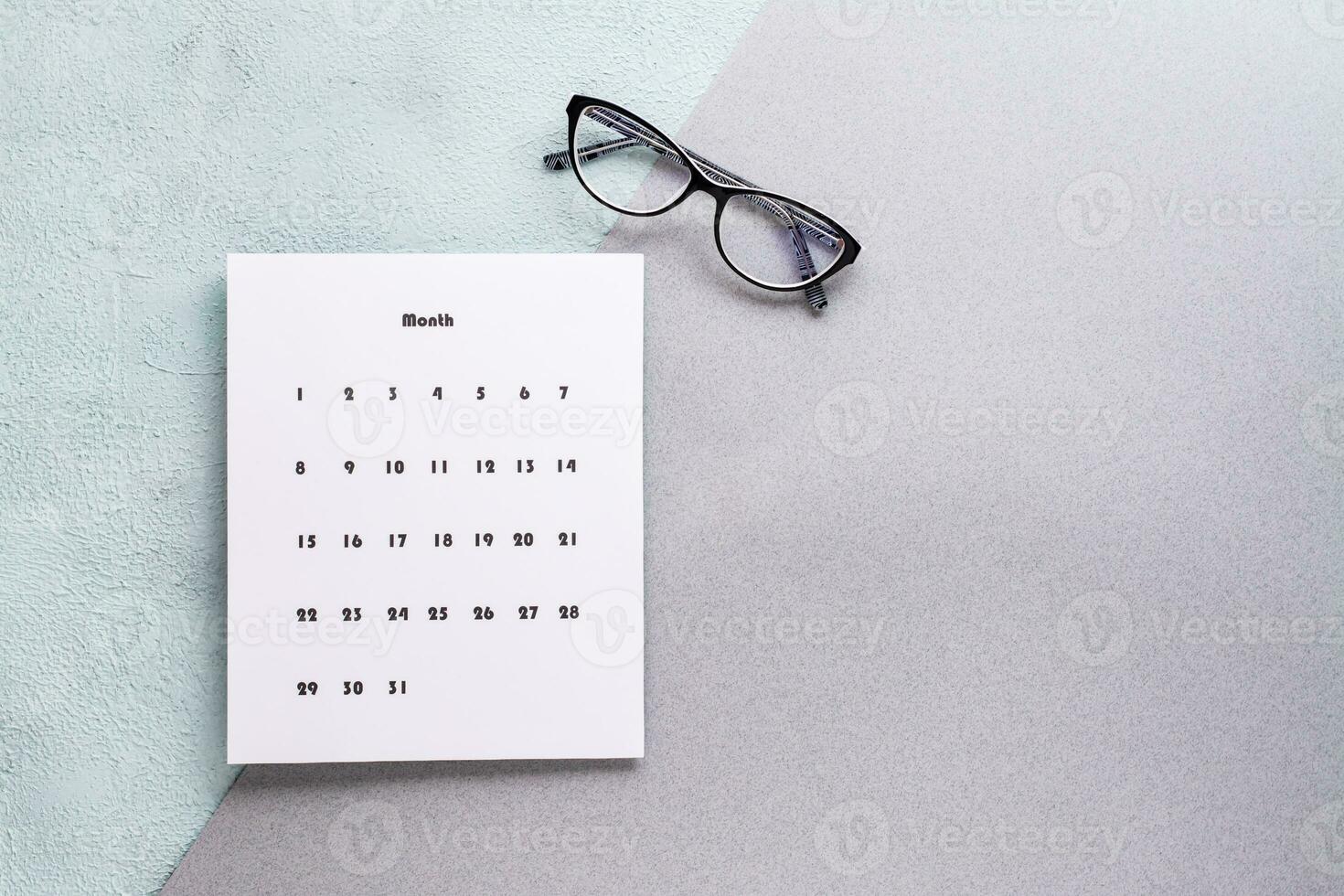 Blank sheet of monthly calendar and glasses on a textured background. Time planning and organization. Copy space photo