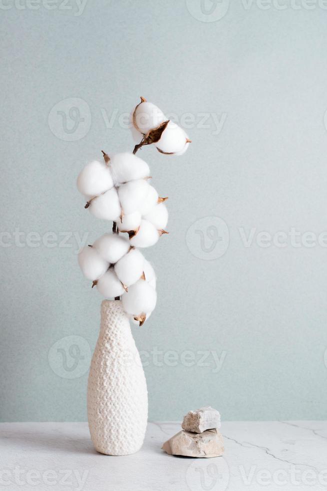 Eco friendly home decor cotton branch in vase and stones on table on gray background. Vertical view photo