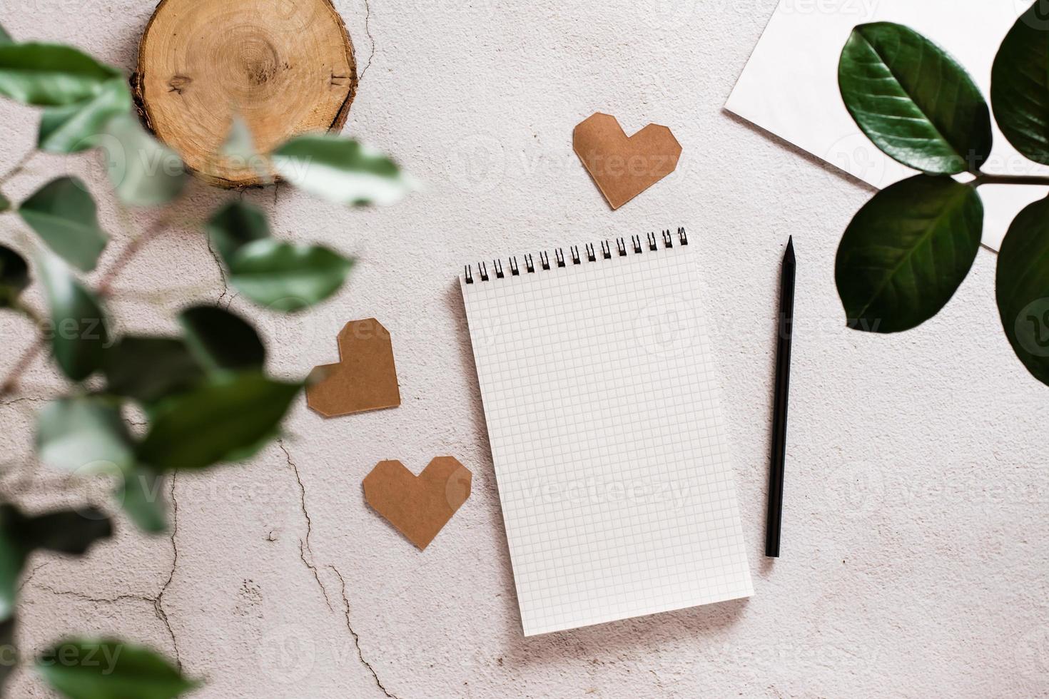 Eco mock up. Open notepad, pencil and craft hearts on a light concrete background and plant home leaves. Top view. photo