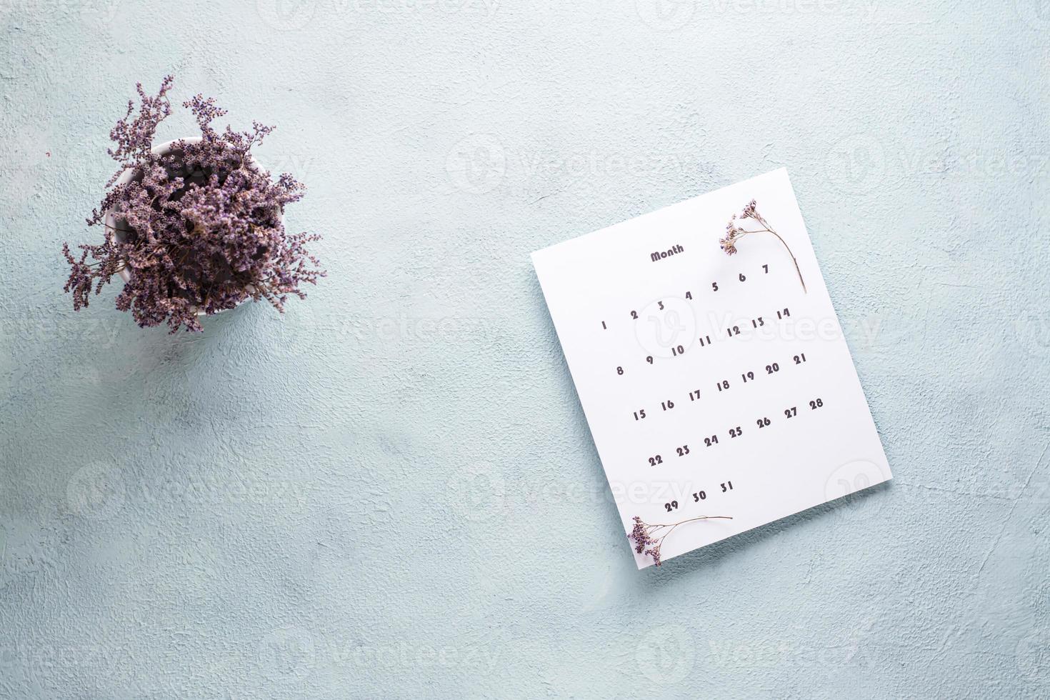 blanco sábana de el mensual calendario y un ramo de flores de seco flores en el mesa. hora planificación y organización foto