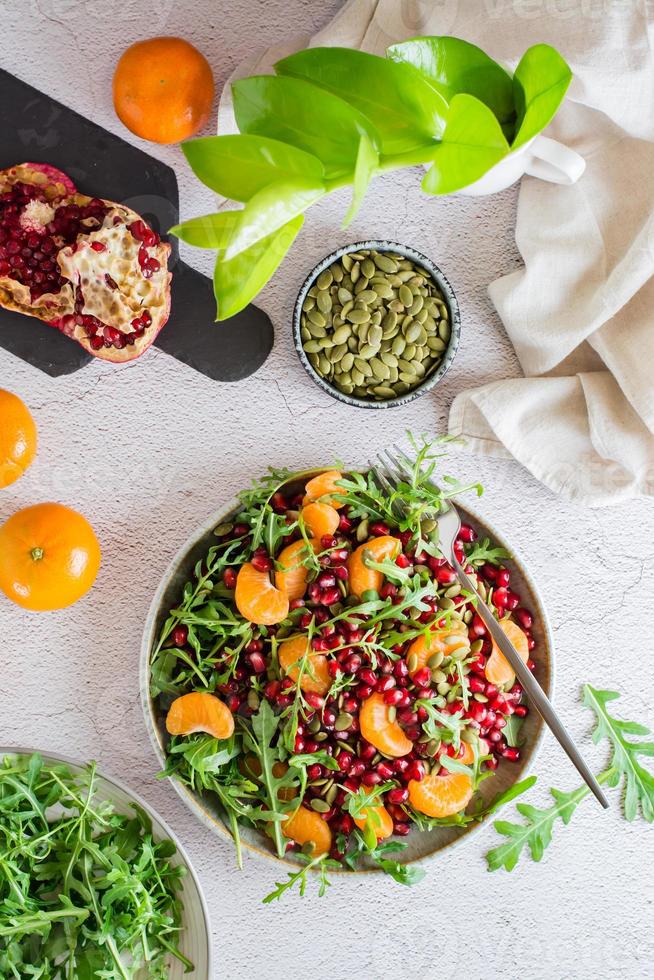 Fruit vitamin salad of pomegranate, tangerine, arugula and pumpkin seeds in a plate on the table. Organic vegetarian food.  Top and vertical view. photo