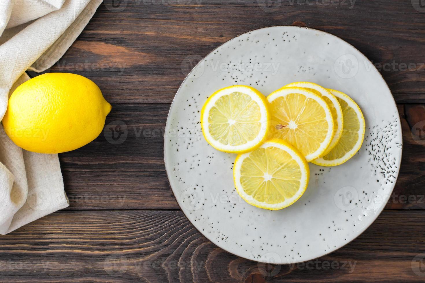 Sliced round pieces of lemon on a plate and a whole lemon next to it on a wooden table. Organic nutrition, source of vitamins. Top view photo