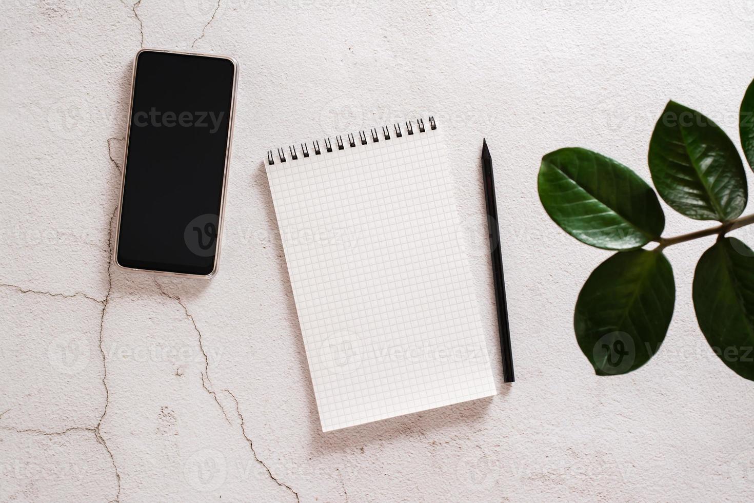 Eco desk. Open notepad, pencil and smartphone on a light concrete background. The concept of choosing means for writing. Top view photo