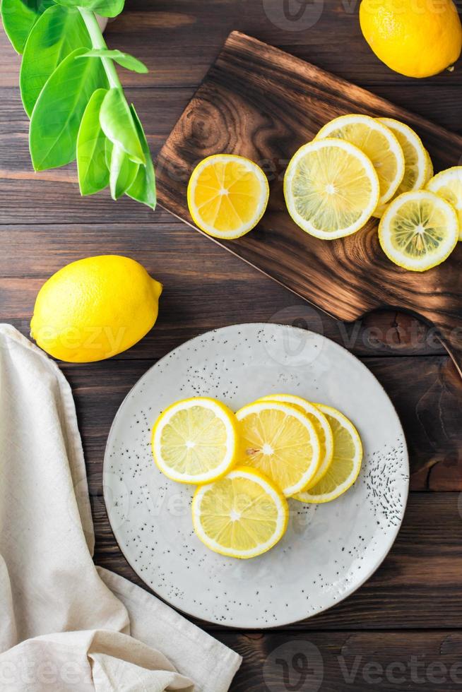 Round pieces of ripe lemons on a plate and on a wooden cutting board on the table. Organic nutrition, source of vitamins. Top and vertical view photo