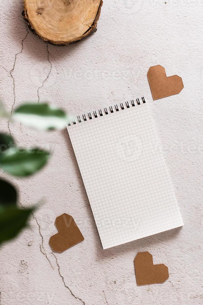 Eco mock up. Open notepad and craft hearts on a light concrete background and plant home leaves. Top and vertical  view. photo