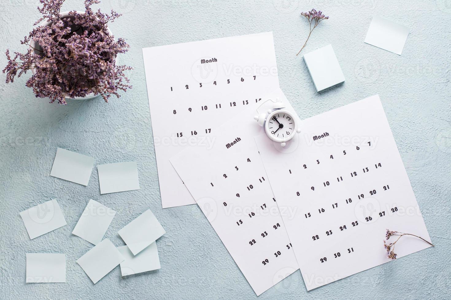 Blank sheets of monthly calendar, alarm clock and a bouquet of dried flowers on the desktop. Time planning and organization photo