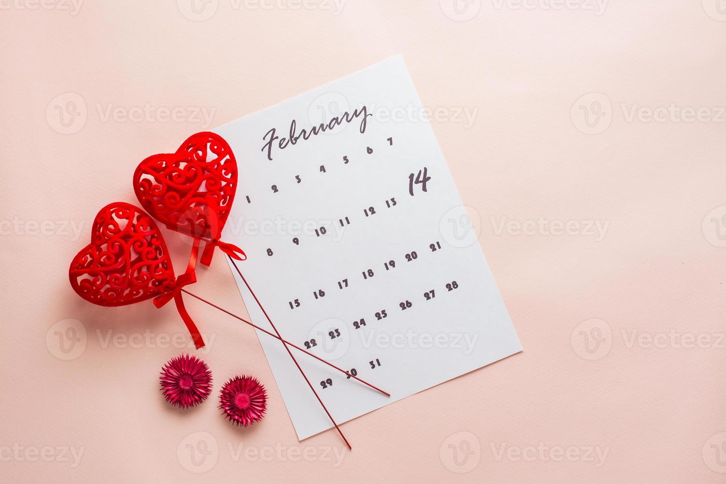 Valentine's Day. Calendar sheet with highlighted date February 14 and two hearts on sticks on a pink background. Top view photo