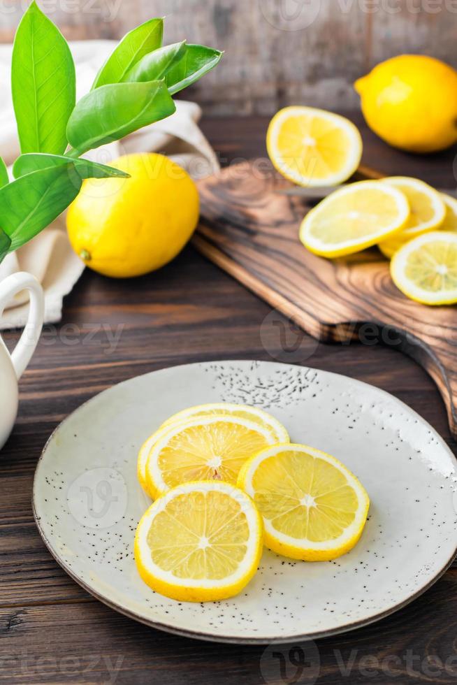 Round pieces of ripe lemons on a plate and on a wooden cutting board on the table. Organic nutrition, source of vitamins. Vertical view photo